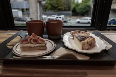 Kafedeki tepside iki fincan kahve, peynirli kek ve incirli tart.