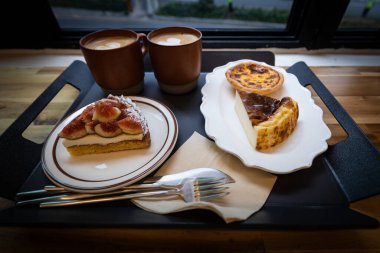 Kafedeki tepside iki fincan kahve, peynirli kek ve incirli tart.