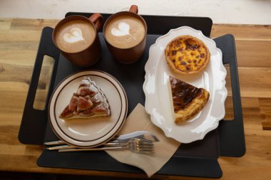 Kafedeki tepside iki fincan kahve, peynirli kek ve incirli tart.