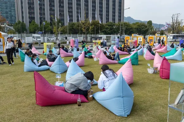 Yeşil çimenlikteki kütüphanede oturan insanlar Güney Kore 'nin göbeğindeki puf minderler hakkında kitaplar okuyorlar.