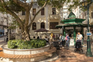 Portekiz tarzı küçük bir meydan ve Macau eski kasabasında bir kafe, insanlar ağacın altındaki kafede.