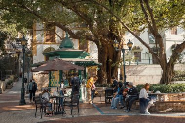 Portekiz tarzı küçük bir meydan ve Macau eski kasabasında bir kafe, insanlar ağacın altındaki kafede.