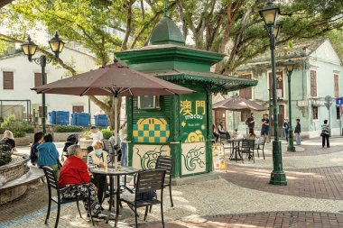 Portekiz tarzı küçük bir meydan ve Macau eski kasabasında bir kafe, insanlar ağacın altındaki kafede.