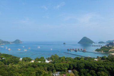 Endonezya 'nın Labuan Bajo kasabası Komodo' da su üzerinde kulübeleri olan tepelerin ve körfezin havadan görüntüsü.