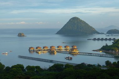 Endonezya 'nın Labuan Bajo kasabası Komodo' da su üzerinde kulübeleri olan tepelerin ve körfezin havadan görüntüsü.