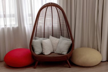 Şık bir rattan yumurta koltuğu, yumuşak yastıklar ve akan perdeleri olan renkli bir pencerenin yanında puf puflar olan rahat okuma köşesi.