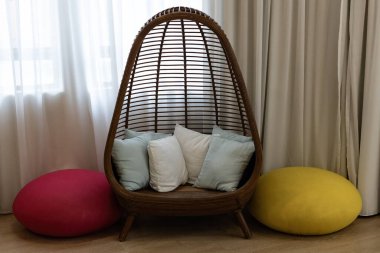 Şık bir rattan yumurta koltuğu, yumuşak yastıklar ve akan perdeleri olan renkli bir pencerenin yanında puf puflar olan rahat okuma köşesi.