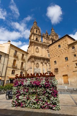 SALAMANCA, İspanya - 3 Temmuz 2024: Clereca Kilisesi 'nin Barok kuleleri, İspanya' nın Salamanca kentindeki ikonik Casa de las Conchas 'ın yanında yükseliyor.