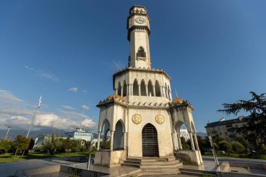 BATUMI, GEORGIA - 15 Ağustos 2024: Gürcistan 'ın Batumi kentindeki tarihi saat kulesi, modern gökdelenlerin ve arka planda güneşin battığı bir halk meydanında duruyor
