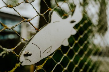 Bavyera 'daki Chiemsee Gölü' nün yakınındaki bir balıkçı yatında metal bir çitte süslü bir balık. Huzurlu göl manzarası Bavyera doğasının, balıkçılık ve tekne kültürünün cazibesini yansıtıyor..