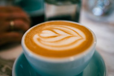 Sıcak bir fincan kremalı kapuçino üzerine narin süt köpüğü, mükemmel bir şekilde ekspreso ile harmanlanmış aroma, tat ve mavi bardaklı tasarım..