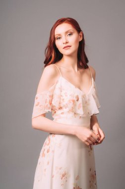 Çiçek desenli bej bir gece elbisesi giyen çekici genç bayan. Romantik kızıl kadının stüdyo portresi. Koyu yakalı, şık görünümlü Bardot Maxi elbisesi. Şehvetli kadın yaz kıyafeti