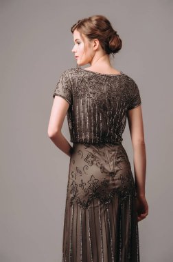 Koyu kahverengi kolları olan boncuklu bir elbise. Klasik tarzda şık, uzun bir gece elbisesi. Genç ve güzel bir kadının stüdyo portresi. Kadın göz kamaştırıcı parlak kıyafet. Modern nedimeler...