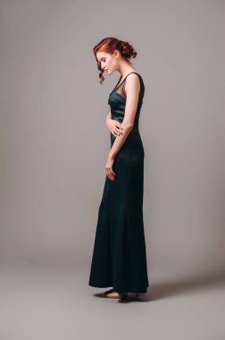 Zümrüt yeşili Maxi gece elbisesi. Şehvetli genç bayanın dokunaklı portresi, seksi görünüş, doğal kızıl kıvırcık saç. Kadınların modern yetişkin modası. Sevimli, uzun kolsuz, düzenli, formalı bir elbise..