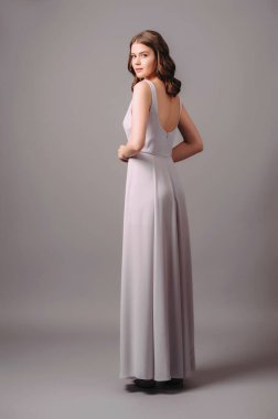 Koyu kahverengi kolları olan boncuklu bir elbise. Klasik tarzda şık, uzun bir gece elbisesi. Genç ve güzel bir kadının stüdyo portresi. Kadın göz kamaştırıcı parlak kıyafet. Modern nedimeler...