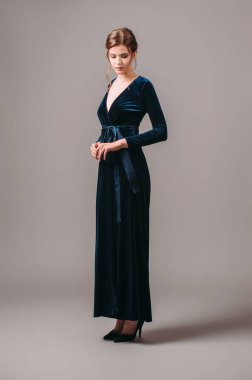 Maksimum kadife gece elbisesini lacivert ile sar. Papyon düğümlü uzun kollu kadife bir elbise. Yüksek topuklu şık bir genç kadının stüdyo portresi, bir etkinlik için şık kıyafetler. Romantik esmer kadın.