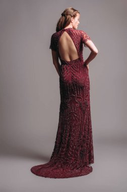 Boncuklu süslü, kısa kollu, kestane rengi kesimli bir maksi elbise. Sırtında trenle kırmızı şeffaf gece elbisesi. Güzel, esmer bir kadının stüdyo portresi. Kadın zarif elbiseler.. 