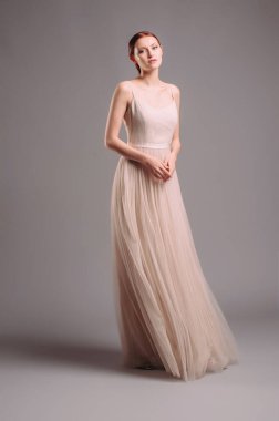 Fildişi Maxi elbiseli çekici genç bir kadın. Yüksek topuklularla dans eden kızıl saçlı kadının stüdyo portresi. Nedimeler bekarlığa veda partisi arıyor. Uçan şifon etekli kolsuz korse.