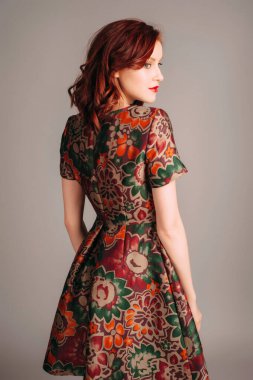 Kahverengi gece elbisesi giymiş güzel kızıl genç bir kadının stüdyo portresi. Zarif moda parlak sonbahar renkleriyle görünür. Jacquard, çiçekli mini elbise, dar kesim, dikiz aynası.