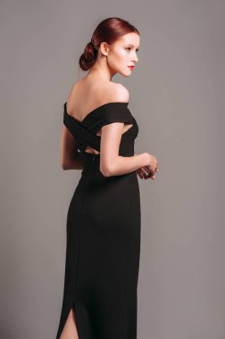 Çapraz siyah elbiseli baştan çıkarıcı genç kızıl kadın, yakın portre. Gri stüdyoda gece elbisesi çıkarılmış. Etkinlik için çekici ince gece kıyafeti. Zarif kadınsı moda.