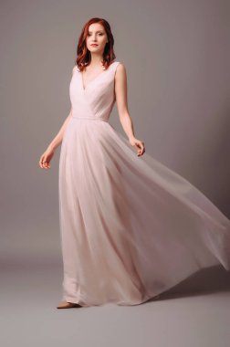 Baştan çıkarıcı kızıl kadın, çapraz pembe tül gelinlik içinde yürüyor. Çekici genç kızıl saçlı gelin. Güzel, uzun kolsuz, atlama yakalı, etekli bir elbise. Zarif gelinlik kadınsı görünümü