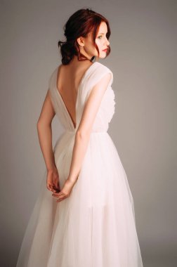 Zarif beyaz gelinlik. Kırmızı dudaklı, sırt dekolteli bir gelinin stüdyo portresi. Kıvırcık saçlı, romantik bir bayan. Bohem gelinlik tarzı. Mutlu evlilikler. Baştan çıkarıcı görünüş