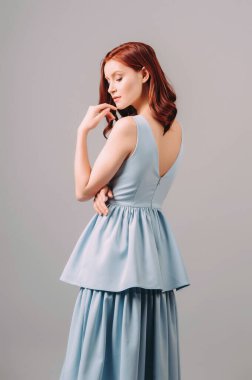 Mavi gece elbisesi giymiş kızıl saçlı kadının şehvetli bir portresi. Doğal makyaj ve kıvırcık saç stili. Yazın kadınsı görünüm, nedime modası, bekarlığa veda partisi için görünüm. Katmanlı etekli kolsuz elbise.