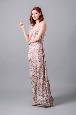 Çiçek desenli, yaka desenli bir yaz elbisesi. V yakalı, kolsuz, çiçek desenli uzun elbisesi olan güzel, mutlu, kızıl saçlı kadın. Baştan çıkarıcı moda kıyafeti