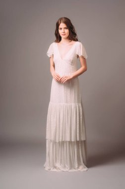 Beyaz parlak dekolteli maksimum yaka elbise ve katlı etek. Kısa kollu, bohem bir gece elbisesi giymiş esmer bir kadının romantik portresi. Nedime modası. Yaz kadınsı görünüm bekârlığa veda partisi
