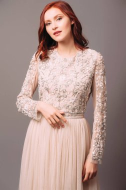 Fildişi uzun kollu Maxi gelinlik. Çiçekli nakış ve tül etekli şeffaf korse. Mutlu kızıl saçlı gelinin şehvetli portresi. Moda bir gelin saç stili ve makyaj. Nedimenin görünüşü