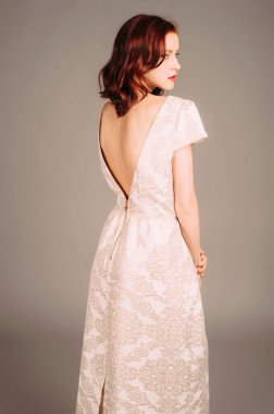 Fildişi renkli kısa kollu gece elbisesi. Kıvırcık saçlı ve kırmızı dudaklı muhteşem genç bayan. Zarif sırt dekolteli nedime elbisesi. Stüdyoda bej elbiseli baştan çıkarıcı kızıl kadın.