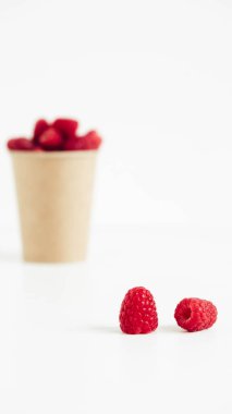 Fresh red raspberries in a paper cup on a white table background.