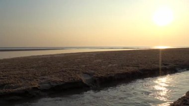 Sahil manzarası sabah güneşiyle, güneş ışığı kuma vuruyor ve insanlar yürüyor ve koşuyor..