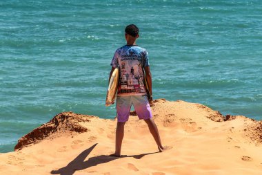 Canoa Quebrada, Brezilya - 05 Aralık 2024: Brezilya 'nın Ceara eyaleti Canoa Quebrada' da Canoa Quebrada Sahili 'nde kaya oluşumları üzerinde duran sörfçü