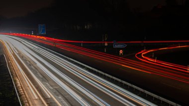 Long exposure, white front and red rear lights as car light strips at night, German text for exit and diverse place names