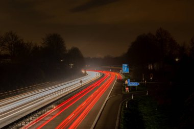 Long exposure, white front and red rear lights as car light strips at night, German text for exit and diverse place names