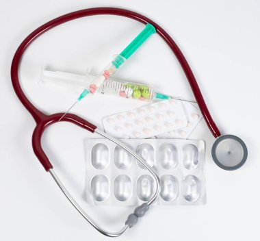 Beyaz arkaplanda renkli tabletlerle stetoskop ve tek kullanımlık şırınga