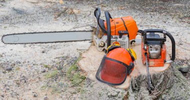 Elektrikli testere ve güvenlik kaskı ağaç kesildikten sonra kütüğün üzerinde duruyor.