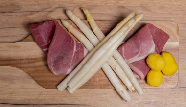 Tahta tabakta taze jambon ve patates ile beyaz kuşkonmaz.