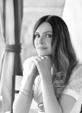 Beyaz tişörtlü güzel esmer bir kızın siyah beyaz portresi. Yazlık bir kafede oturan mavi gözlü. Kahve molası. Tatil kavramı