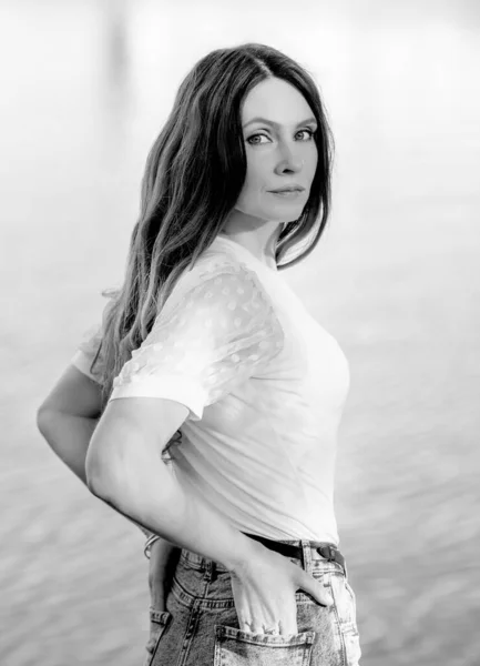 Black and white portrait of a beautiful brunette girl in a white T-shirt and jeans near the river. Summer. Relax. Camping concept
