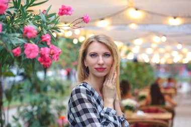 Zarif görünüşlü, sarışın, beyaz bir kadının portresi olan pankart. Arka planda bir yazlık kafe ve arka planda Bokeh ışıkları var. Kadınlık kavramı