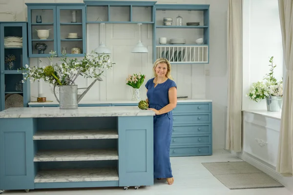 Woman housewife in a blue dress in a cozy modern kitchen. Home and happiness conc.