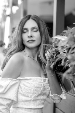 Siyah beyaz bir portre ve güzel bir esmer gözlerini kırmızı çiçeklerin yanında kapatıyor. Beyaz elbise ve kırmızı ruj. Makyaj ve cilt bakımı. Kadın konsepti