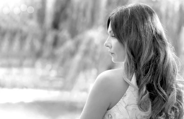 Black and white banner with a young caucasian girl in a summer dress with a floral print, view from the back. Background - park in summer. Women concept. Copy space on the left