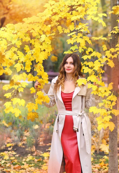 appy girl in a beige raincoat and red dress walking in the autumn park. City. Autumn and relaxation