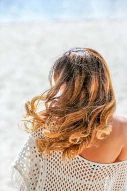 Doğanın arka planında bukleleri olan güzel esmer kız. Arkadan bak. Örgü beyaz pareo. Saç bakımı. Güzellik konsepti.