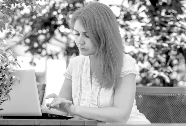 一个年轻女人在街上的一家夏季咖啡店里拿着笔记本电脑工作的黑白照片 在室外工作商业概念 — 图库照片