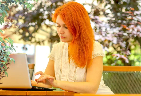 这个女孩在街上的一家夏季咖啡馆里的笔记本电脑后面工作 商业概念 — 图库照片