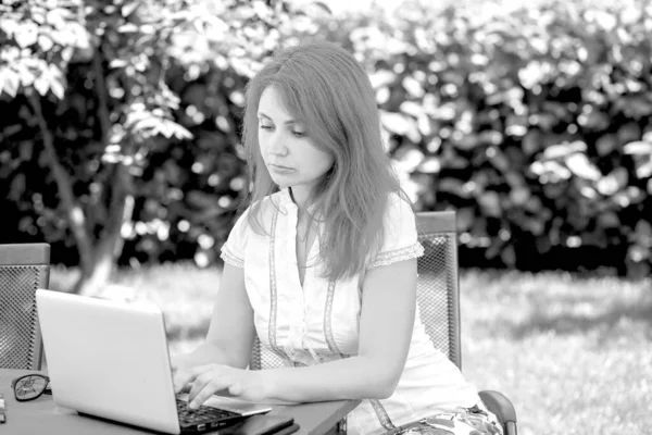 一个年轻女人在街上的一家夏季咖啡店里拿着笔记本电脑工作的黑白照片 在室外工作商业概念 — 图库照片